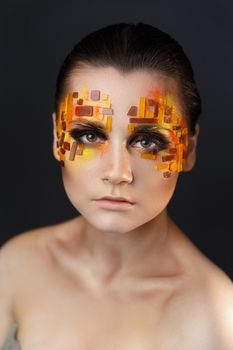 Portrait of a girl with an original make-up. Beauty close-up with orange and red rhinestones on a face of the model