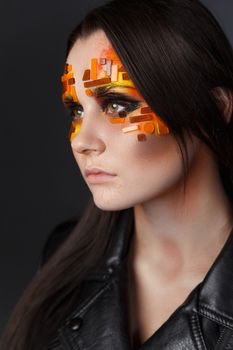 Portrait of a girl with an original make-up. Beauty close-up with orange and red rhinestones on a face of the model