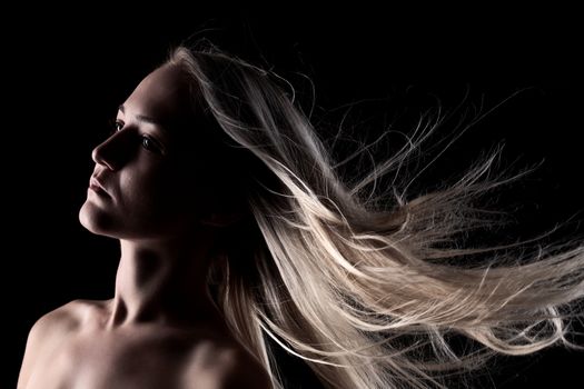 portrait of a blond girl with windy hair, on black background