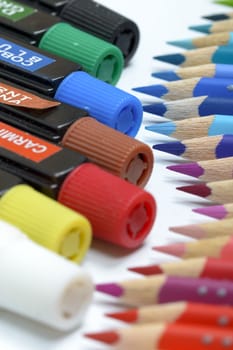 Bundle of colored pencils and tubes of paint on the colorful background