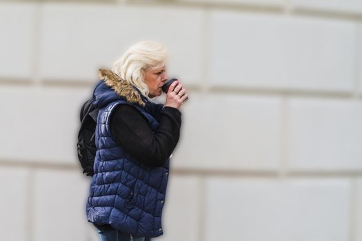 Side portrait of a blonde woman with a coffee to go.