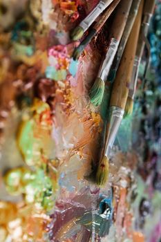 artists brushes and oil paints on wooden palette. macro artist's palette, texture mixed oil paints in different colors and saturation. palette with paintbrush and palette-knife