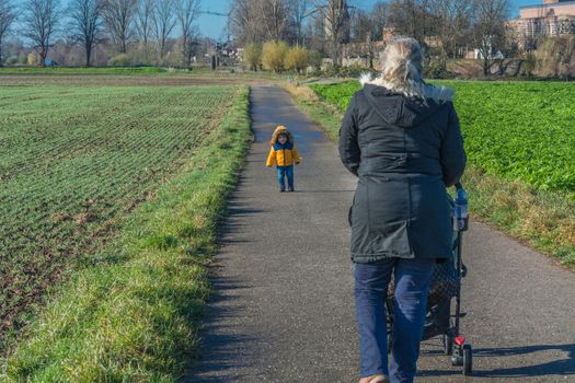 Grandmother with grandson while walking and pushes a baby carriage.