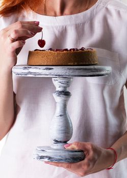 Woman's hands hold a  cheesecake on a wooden cake stand.Cheesecake decorated with cherry sauce with berries 