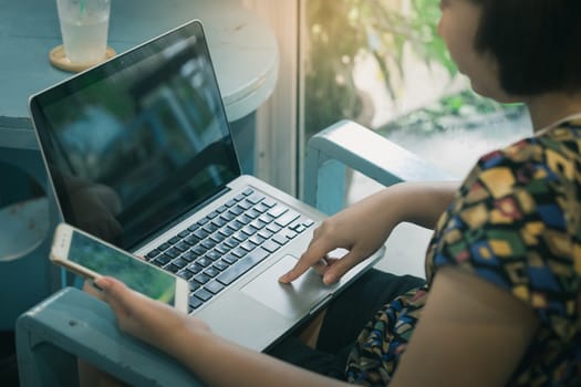 Woman forefinger press button on laptop computer while another hand holding smartphone for electronic shopping. E-commerce business at home concept with vintage filter effect