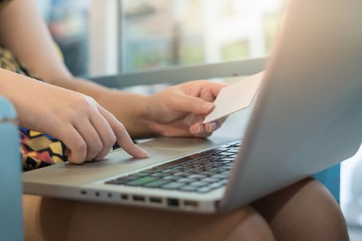 Woman forefinger press button on laptop computer while another hand holding credit card for electronic shopping payment. E-commerce business at home concept.