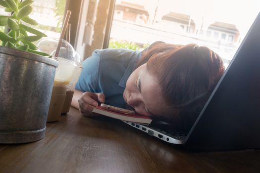 Young Hipster woman sleeping while working working with laptop computer in coffee shop. exhausted worker on busy day. Freelance business activity concept.