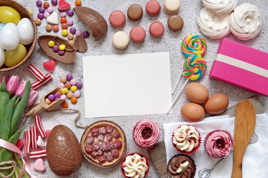 Selection of easter sweets, bakery cupcakes, chocolate eggs and confectionery with a blank piece of paper in the centre 