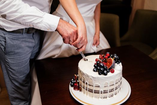 Newlyweds cut the wedding cake decorated with fresh fruits. Bride and groom cut  wedding cake