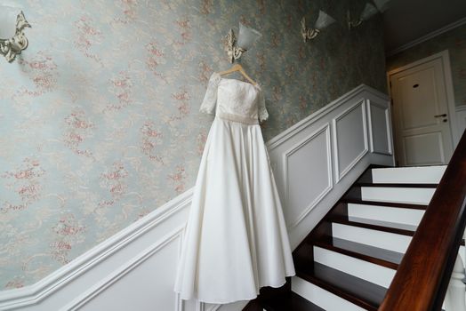 Cream bride dress hang on the lamp against the wall next to the stairs in the hotel