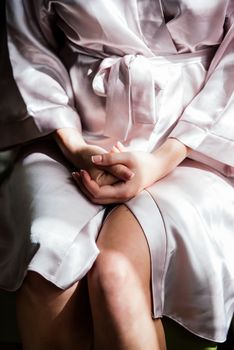 A girl in a silk robe sits on a chair and crosses her hands on her knees.