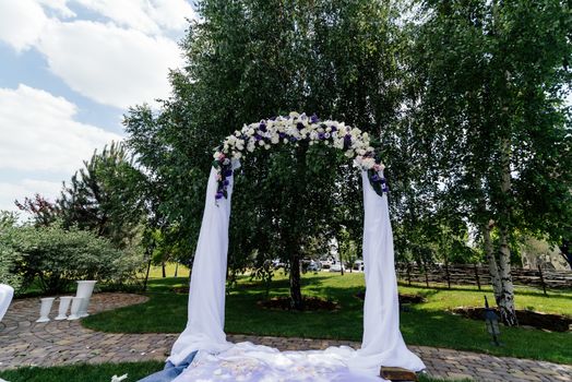 Wedding arch with flowers and white cloth near the birch