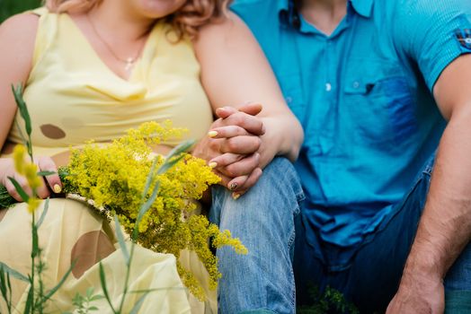 Man in blue clothes and woman in yellow dress are sitting and holding hands