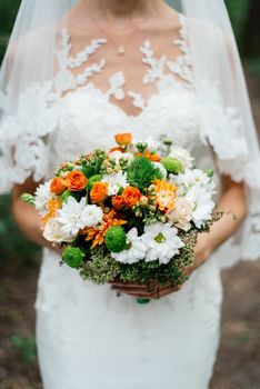 Wedding bouquet of orange roses, white and orange chrysanthemums and greenery in the bride's hands