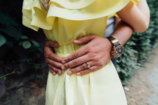 Man's hands on the waist of a girl in yellow dress. Man holds his hands on girl's waist . A loving couple