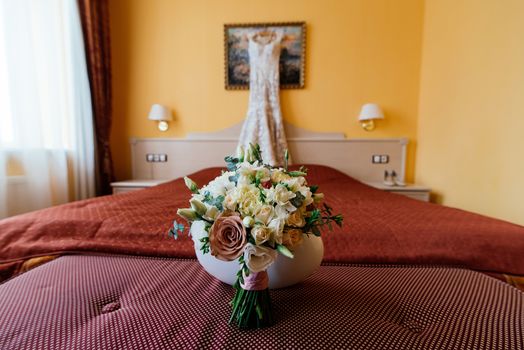 Beautiful lush wedding bouquet on a bed in a bride's bedroom with blured wedding dress in the background