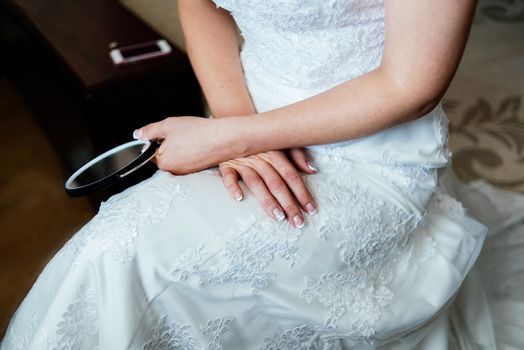 Bride in white wedding dress is sitting and holding a mirror