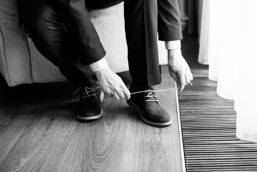 The groom is sitting and tying the laces on shoes