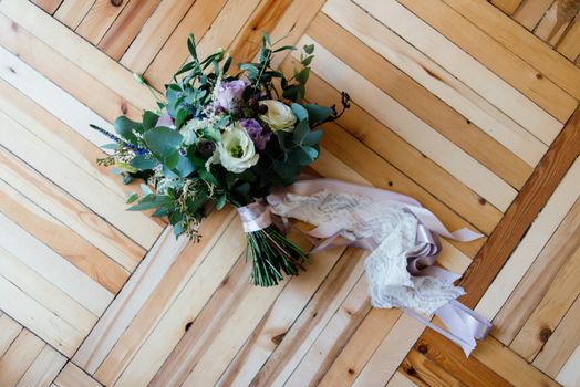 Wedding bouquet of purple and white flowers tied with ribbons on the parquet