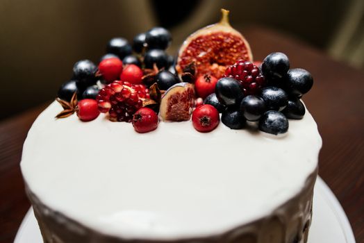 Cake decorated with fresh fruits on the white plate on a wooden table. Wedding cake