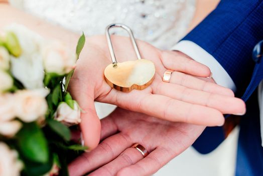 Gold wedding lock in the form of heart in the hands of the bride and groom. 