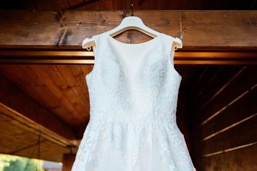 A beautiful cream wedding dress hanging on the wall near the wooden house