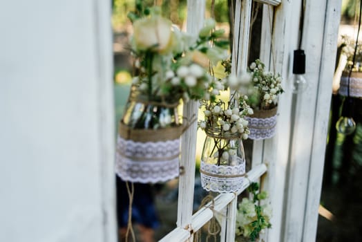 Little wedding floral decorations in rustic style hang in jars decorated with sacking and lace