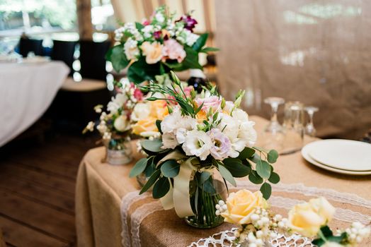 Wedding bouquets of yellow, white and pink roses are in vases on dinner table