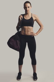 Portrait of sporty young woman posing with a gym bag,  against a gray background