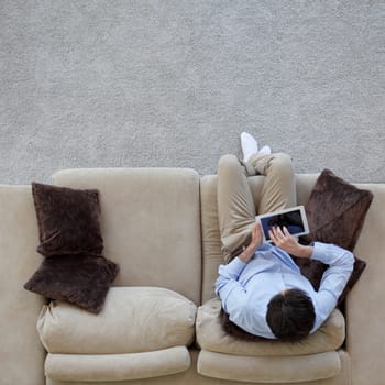Man surfing on tablet on a couch at home, top view