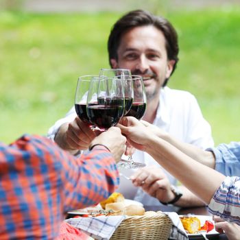 Friends clink glasses of red wine at outdoor dinner