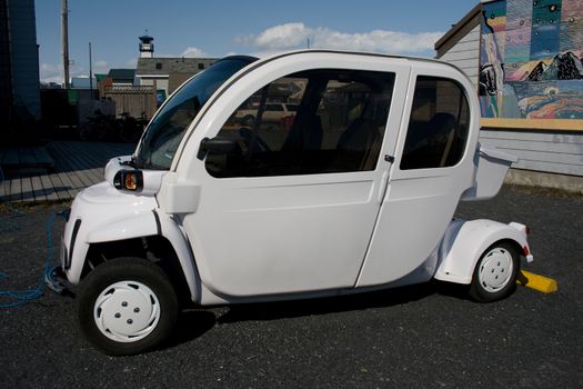 A small white electric car pligged in to charging station. 