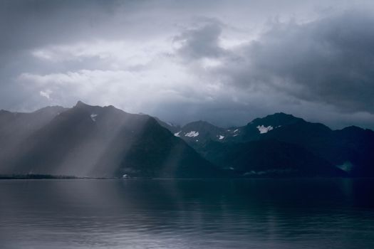Rays of light peak through the clouds in the early morning over the mountains and ocean near Seward, Alaska. 