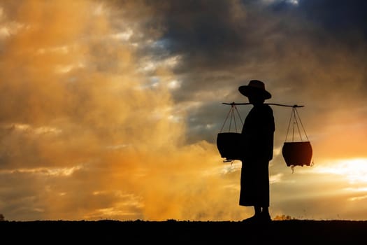 Female farmer walking of basket on fields at sunset.