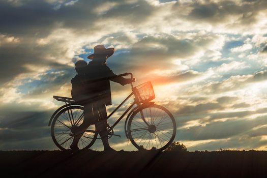 farmer woman with bicycle on a field at the sunset.