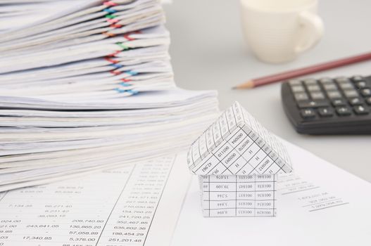 House on finance account have blur pile overload document of report and receipt with colorful paperclip and calculator with pencil and cup of coffee as background.