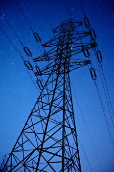 High Voltage Pole During NIght Hours. Clear NIght Sky with Many Stars. Vertical Long Exposure NIght Photography. HIgh Voltage Pylon