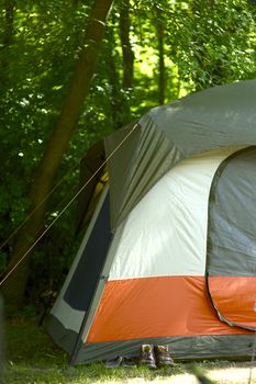 Campsite Tent. Large Green Tent Between Trees. Old Dirty Shoes in Front of the Tent. Campsite  Theme. Vertical Photography.