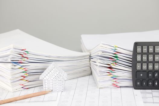 House and pencil on finance account have pile overload document of report and receipt with colorful paperclip and calculator place vertical as background.
