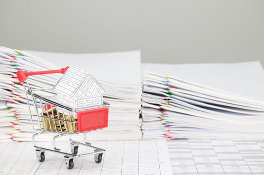 House in shopping cart with gold coins on finance account have blur pile overload document of report and receipt with colorful paperclip as background.