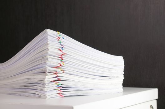 Pile overload paperwork of receipt and report with colorful paperclip on white cabinet with black wall.