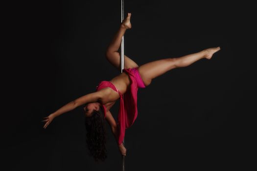 Beautiful woman performing pole dance, studio shot on black background