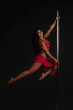 Beautiful woman performing pole dance, studio shot on black background