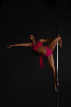 Beautiful woman performing pole dance, studio shot on black background