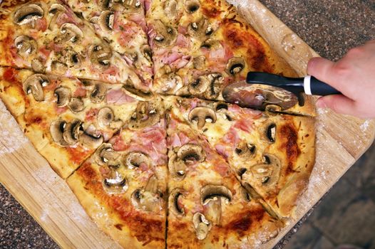 Slicing Fresh Home-Made Pizza. Tasty Pizza Sliced by Female (Hand). Wood Board and Granite Countertop - Top View.