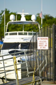 At the Pier - No Trespassing Sign. Violators Subject to Arrest and or Fines. Large Expensive Boat in the Background.