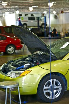 Green Broken Vehicle. Small Car in the Dealer Service. Open Hood. Other Vehicles in the Background.