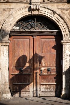 Old European Sturdy Wood Doors with Arch. Old City Lighting and Street Signs Shadow. Daylight Vertical Photography. European Architecture. 
