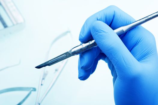 Scalpel in Doctor\'s Hand - Blue Latex Glove. Inside Dental Clinic