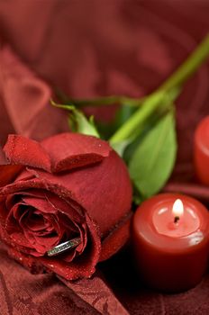 Red Rose Engagement Ring. Red Candles and Soft Burgundy Background Fabric